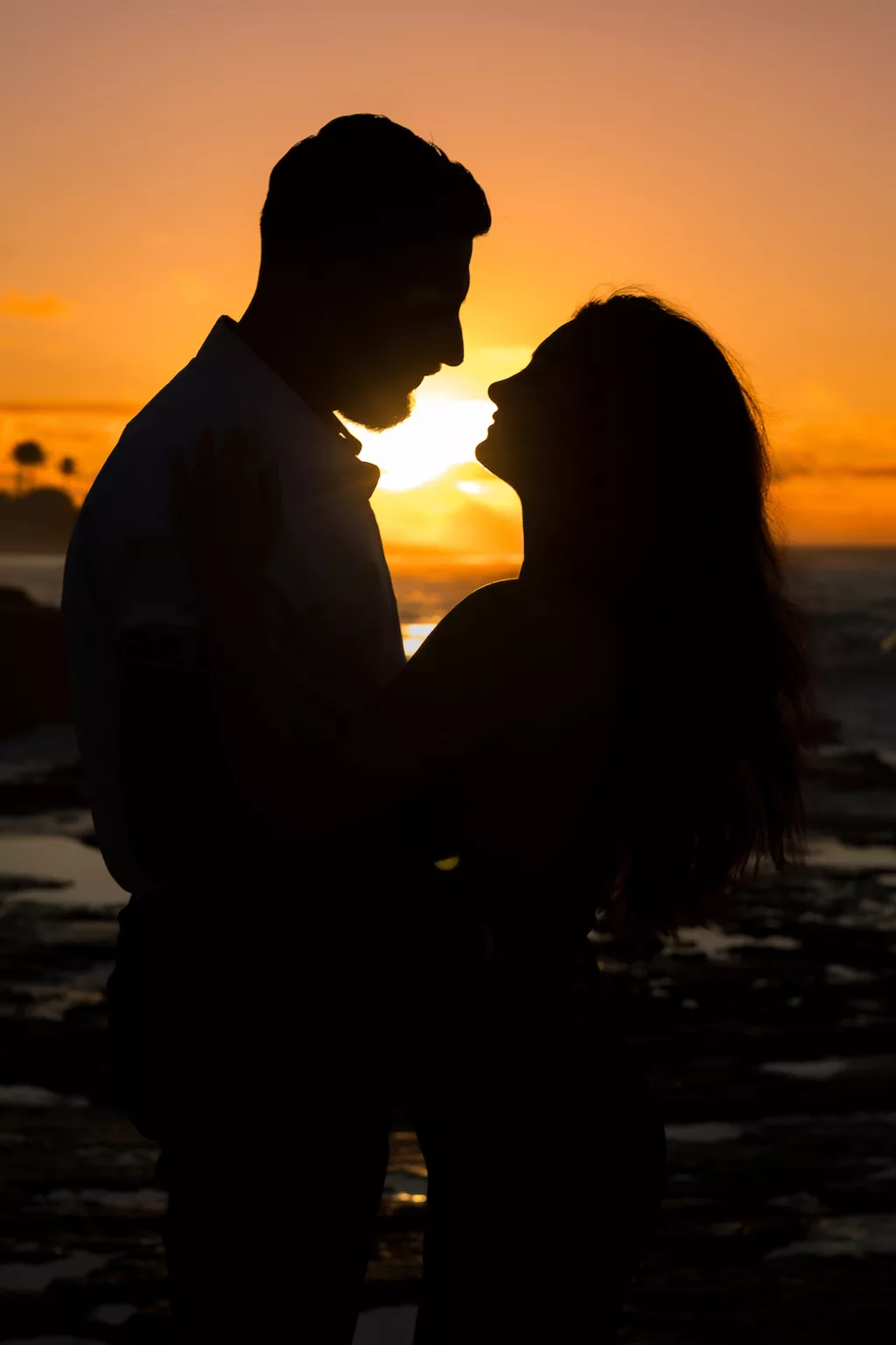 an image of a couple happily smiling at each other in front of a sunset captured by oahu photographer